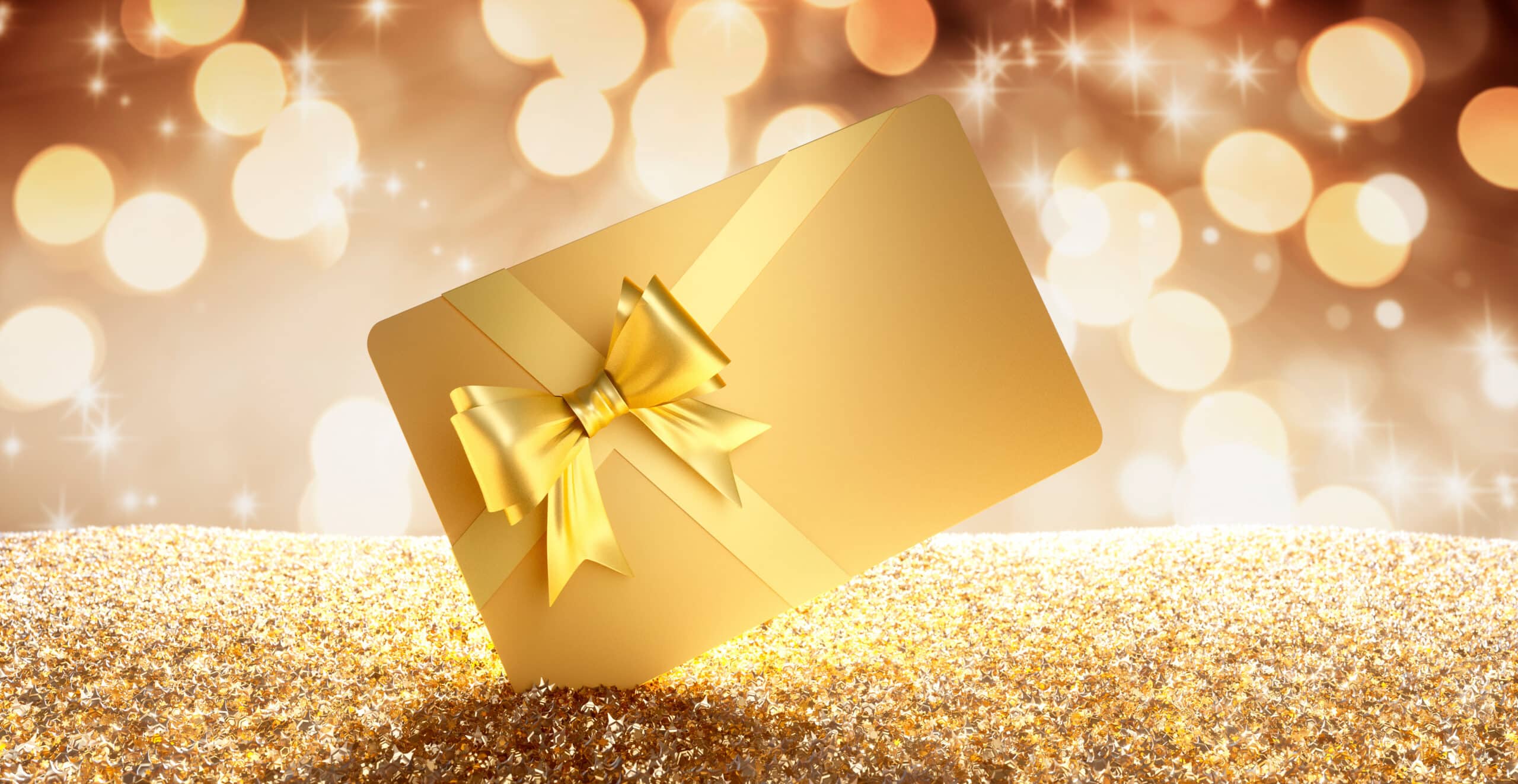 Carte cadeau dorée avec un nœud en ruban satiné, posée sur un tas de confettis dorés en forme d'étoiles, sur fond bokeh festif brun clair.