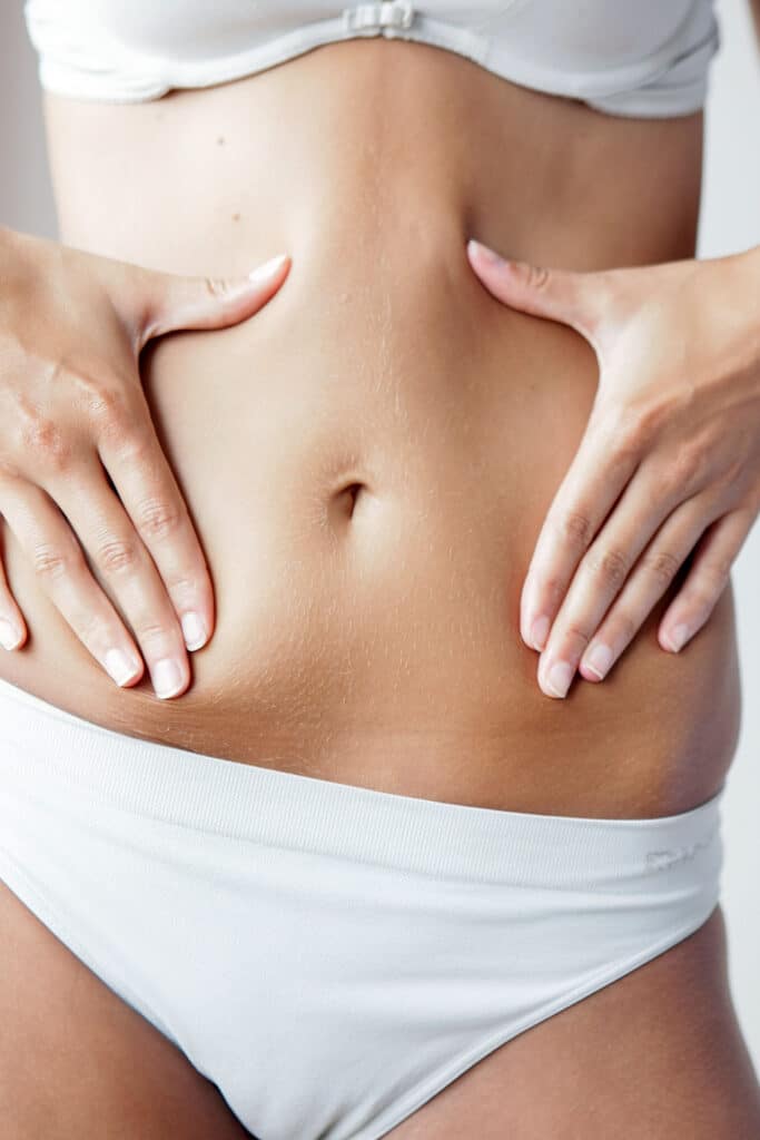 Ventre ferme et mains tenant les flancs : corps féminin Gros plan sur un ventre féminin tonique, mains tenant doucement les flancs, montrant un nombril et un duvet fin, vêtue d'un sous-vêtement blanc.